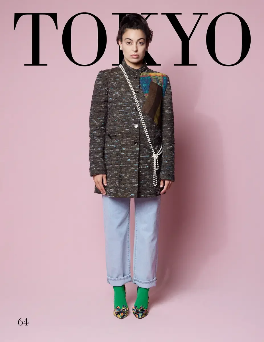 JUS10H 2025 Tokyo lookbook, a female model wearing a dark olive and multicolor flecked boucle tweed coat with colorful plaid and brown tweed patchwork appliqués at the shoulder, a long pearl lariat necklace, light wash wide-leg cuffed denim jeans, gr