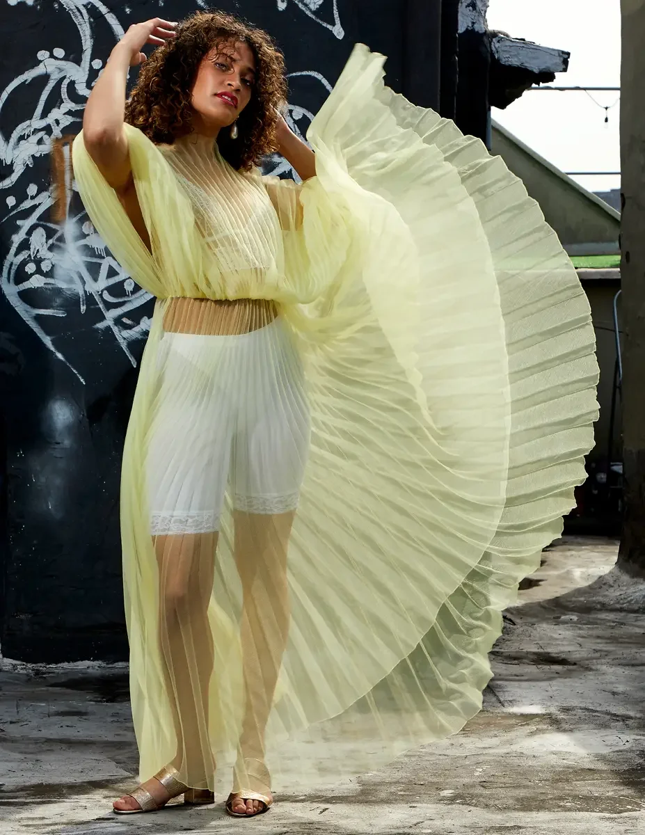 Fashion test shoot, full-length, model Ireland T in J'Amemme yellow pleated sheer gown, Taro Collection earrings, graffiti wall backdrop, East Village rooftop, New York City, styling by Matsine Stinson, makeup by Stefani Paige Vivian, photographed by