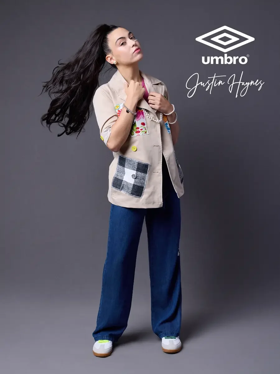 Fashion lifestyle photography for the Umbro France collection. Vanessa in a three-quarter stance with hair in motion holding her collar and gazing upward in a sand utility jacket with floral patchwork panels over a fuchsia t-shirt and wide-leg dark i