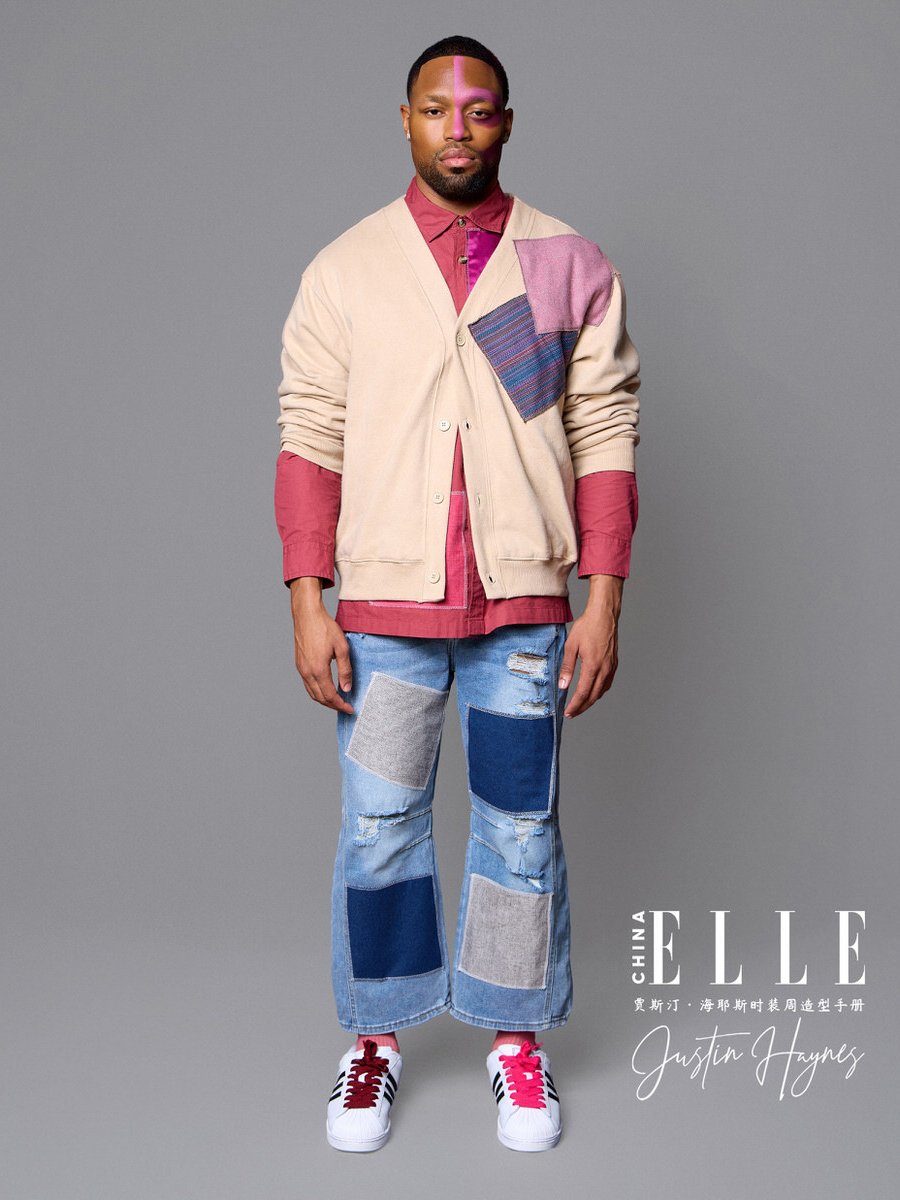 Male model wearing a beige cardigan with colored patchwork, red shirt, wide-legged ripped jeans with patchwork, red and white sneakers, standing against a grey background.
