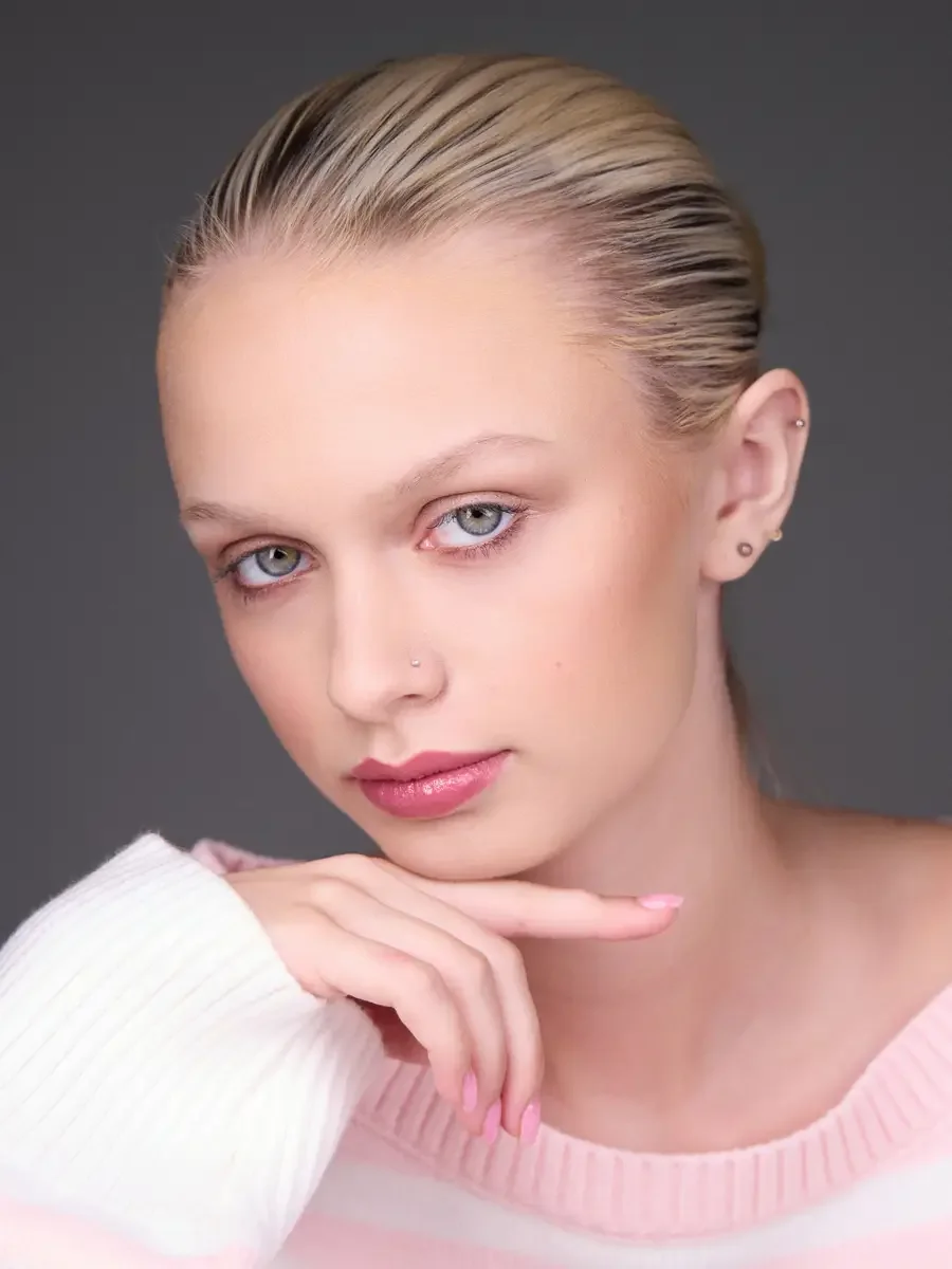 Model portfolio development session, beauty, close-crop, hair slicked back, three-quarter turn, direct gaze, hand at chin, rose lip, soft eye, pink striped sweater, gray background, photographed by Scott Parker Photo, New York