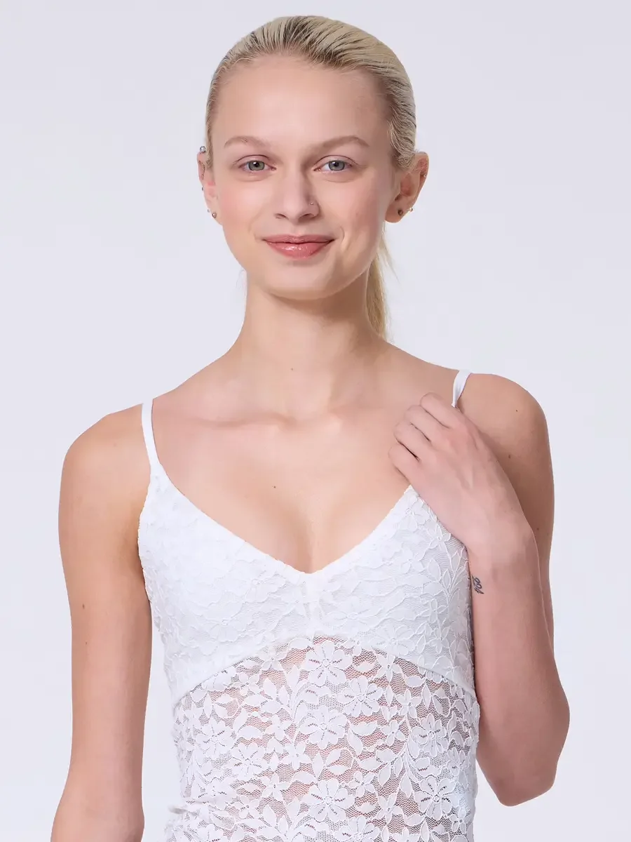 Model portfolio development session, commercial look, white lace crop camisole top with floral lace panel and V-neckline, close-crop, hair pulled back, open smile, one hand raised to shoulder strap, light gray background, photographed by Scott Parker