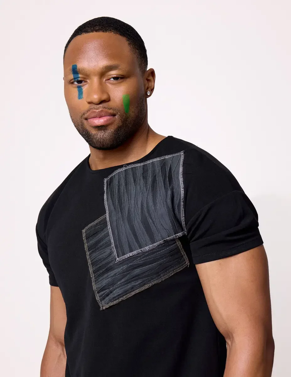JUS10H Black Summer Jacket editorial, close portrait of male model in black fitted tee with large gray patchwork chest detail, three-quarter view, white background, photographed by Scott Parker Photo