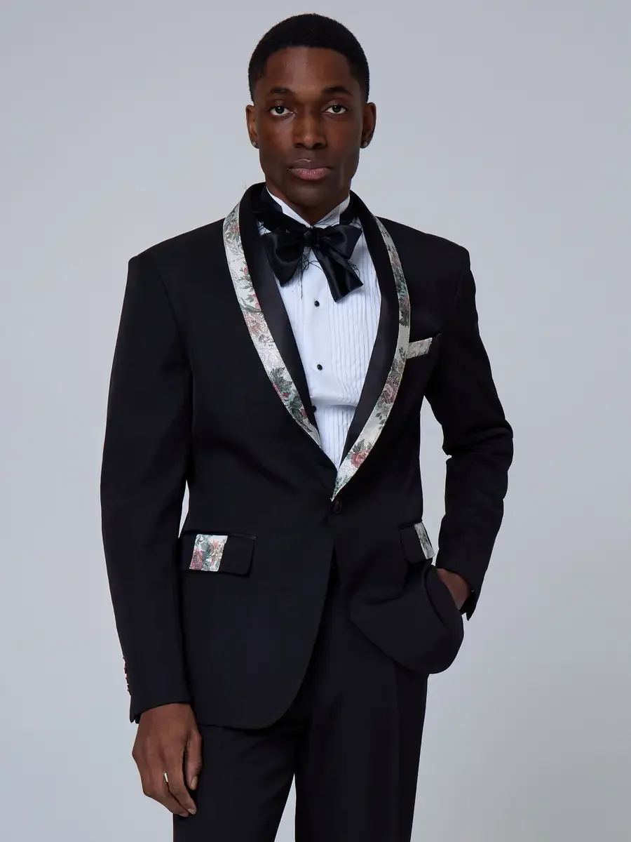 JUS10H 2025 New York Bridal Fashion Week, black single-button tuxedo with floral-print shawl lapels and matching pocket trim, styled with a black satin bow tie and pleated white dress shirt, photographed by Scott Parker Photo