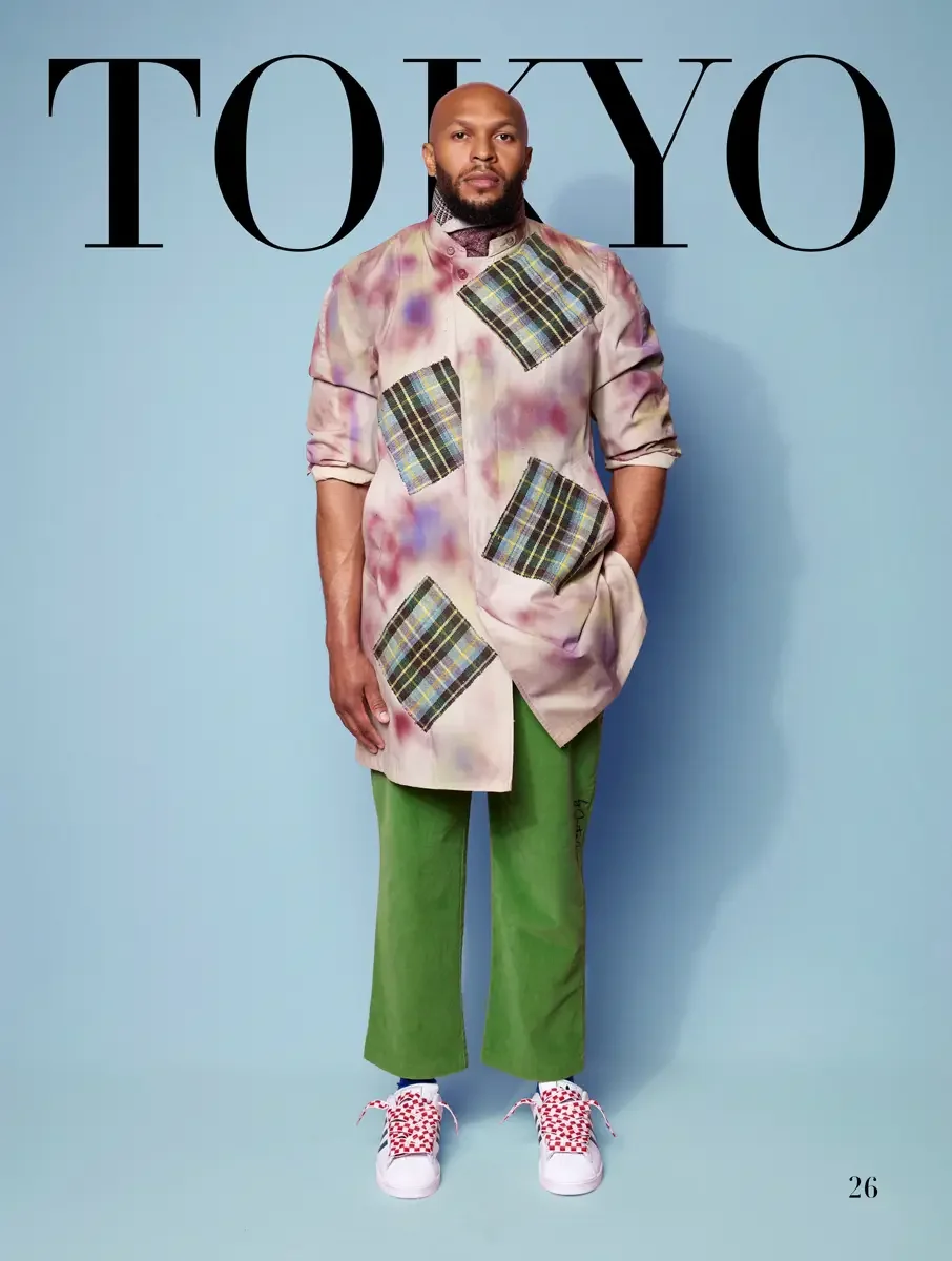 JUS10H 2025 Tokyo lookbook, tie-dye blush longline shirt with large tartan patches over green wide leg trousers and red checkered Adidas sneakers, light blue background, photographed by Scott Parker Photo for the Tokyo Fashion Council