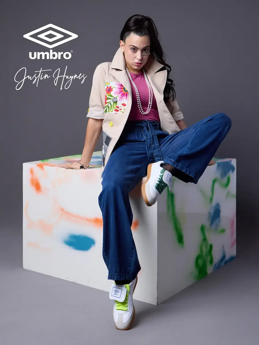  Elevated soccer style for the Umbro France collection. Vanessa seated on a color-splashed prop with arms resting on one knee in a sand utility jacket with floral patchwork panels over a fuchsia t-shirt and wide-leg dark indigo jeans, styled by Justi