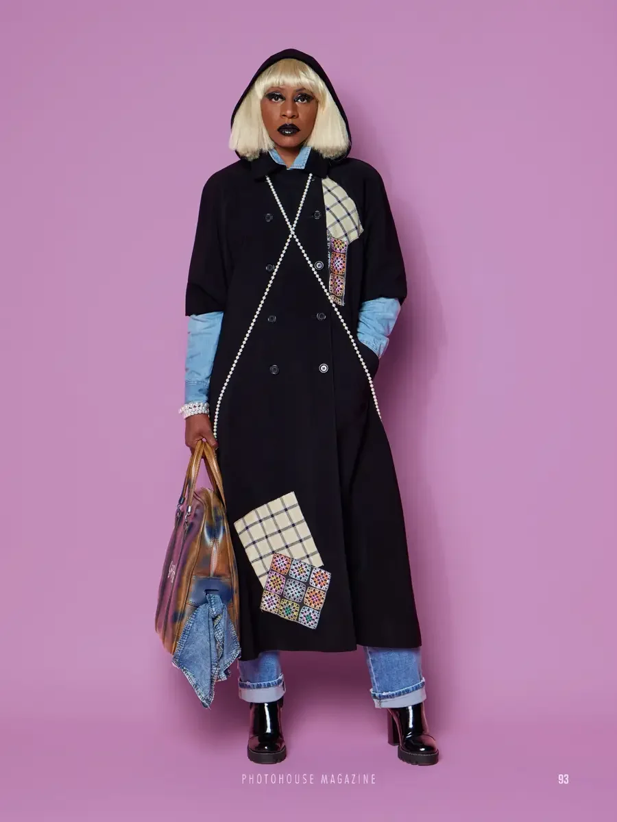 JUS10H 2025 Photohouse Magazine feature, model in black hooded double-breasted longline coat with tartan and multicolor embroidered patchwork panels, pearl rope detail, layered over chambray shirt and cuffed wide-leg jeans, carrying oversized tote, l