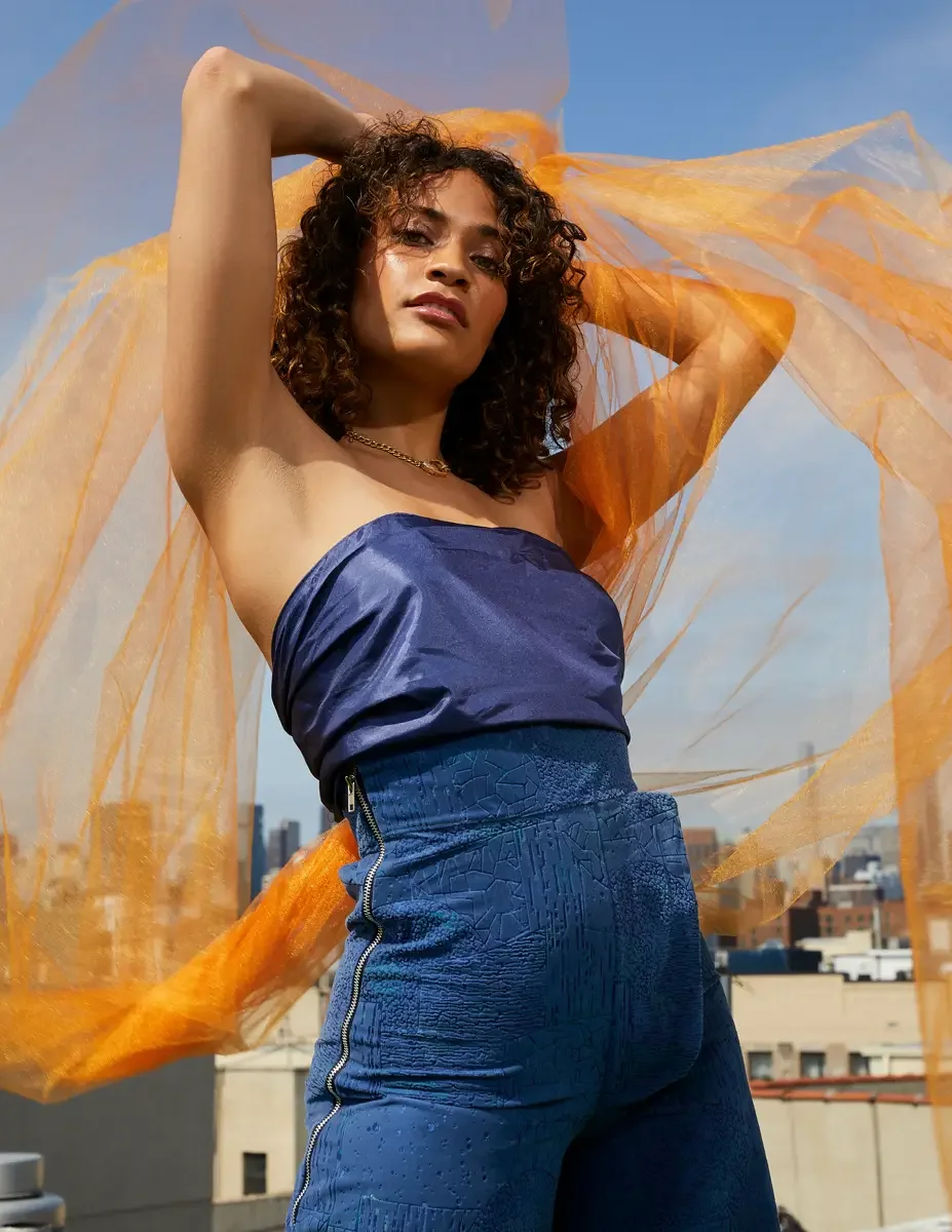 Fashion test shoot, close-up of model Ireland T in Amy Page DeBlasio textured blue wide-leg pants with side zipper detail and navy strapless top, orange tulle, East Village rooftop, New York City, styling by Matsine Stinson, makeup by Stefani Paige V