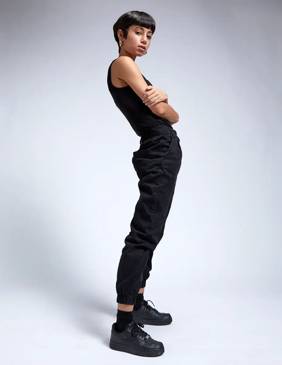 Eloissa, profile, arms crossed, black tank and black cargo jogger pants, gold hoop earrings, East Williamsburg studio test shoot, makeup by Schanica Pickens, photographed by Scott Parker Photo