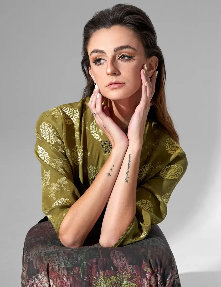 Fashion model Macy, close-up portrait, hair down, hands framing face, olive green satin jacquard top with gold medallion print, script tattoo and star tattoos on inner forearm visible, New York studio test shoot, photographed by Scott Parker Photo
