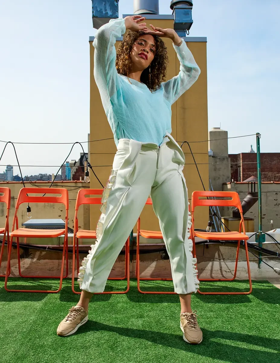 Fashion test shoot, full-length, model Ireland T in Amy Page DeBlasio white ruffle-trim pants with front zipper and aqua sheer knit top, East Village rooftop, New York City, styling by Matsine Stinson, makeup by Stefani Paige Vivian, photographed by 