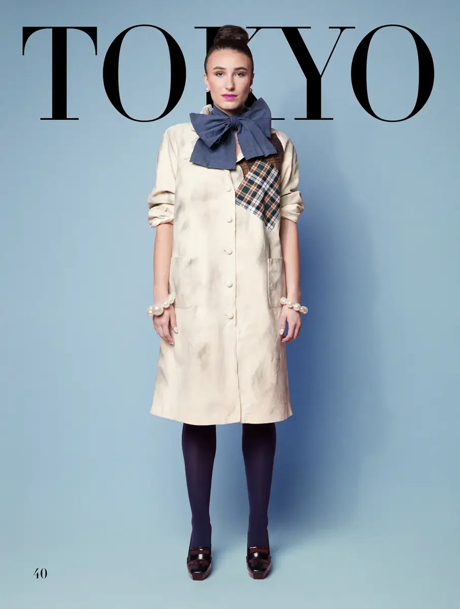 JUS10H 2025 Tokyo lookbook, a model wearing a cream button-front midi coat dress with a plaid patchwork panel at the chest and a large slate blue denim bow at the neckline, styled with pearl bracelets, navy tights, and dark burgundy platform heels, o