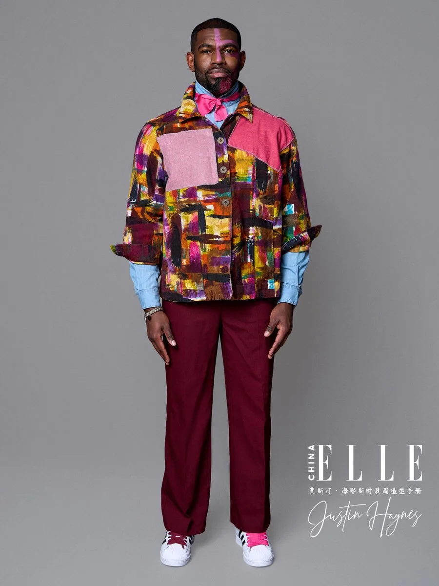 Man wearing a colorful patchwork jacket, maroon pants, white sneakers, and a blue shirt with pink accessories, standing against a plain gray background for Elle China photoshoot.