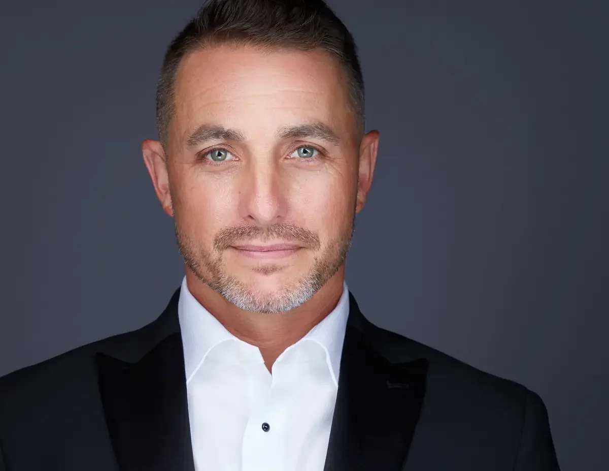 Senior executive portrait, black tuxedo jacket and white shirt, direct composed gaze, gray background, photographed by Scott Parker Photo