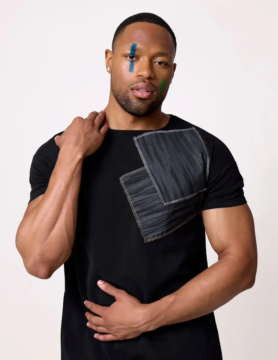 JUS10H Black Summer Jacket editorial, three-quarter portrait of male model in black fitted tee with gray patchwork chest detail, white background, photographed by Scott Parker Photo