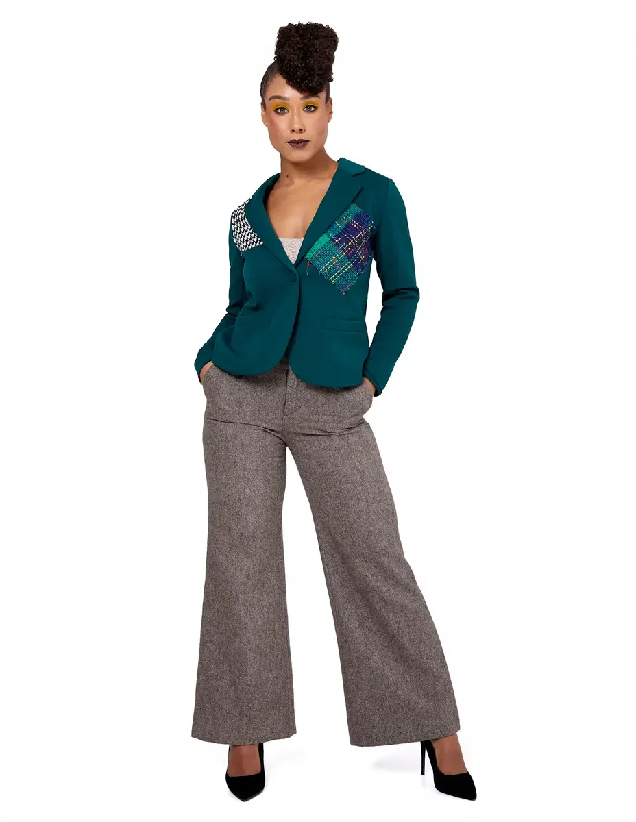 Model portfolio development session, high fashion editorial look, teal single-button blazer with houndstooth and multicolor tweed appliqué panels, wide-leg heatheorange trousers, black stiletto heels, full-length, hands in pockets, direct gaze, white