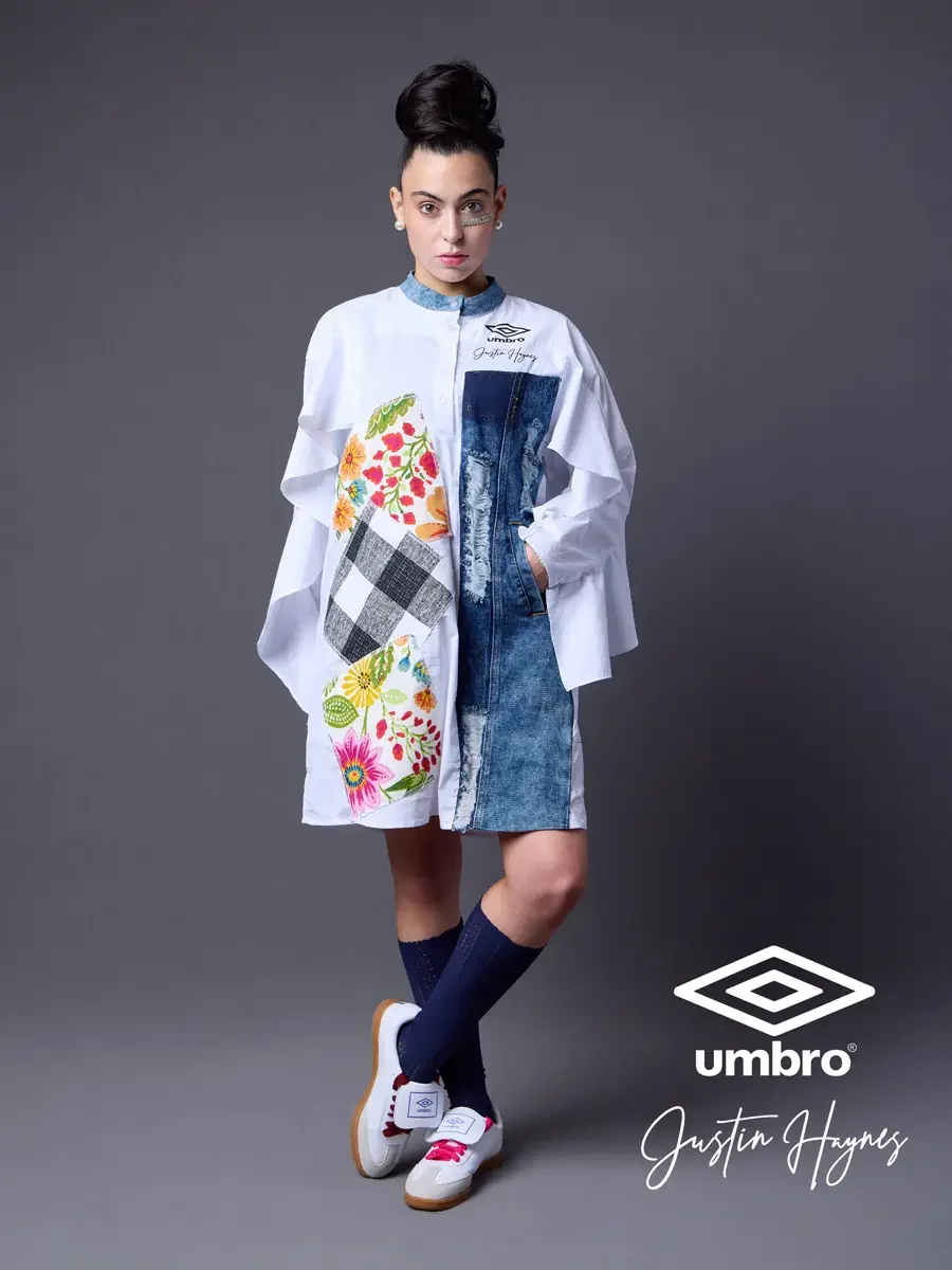  Lookbook photography for the Umbro France collection. Vanessa standing front-facing with sleeves gathered and one leg crossed in an oversized white shirt dress with dramatic ruffled sleeves, a distressed denim center panel, and floral patchwork, sty