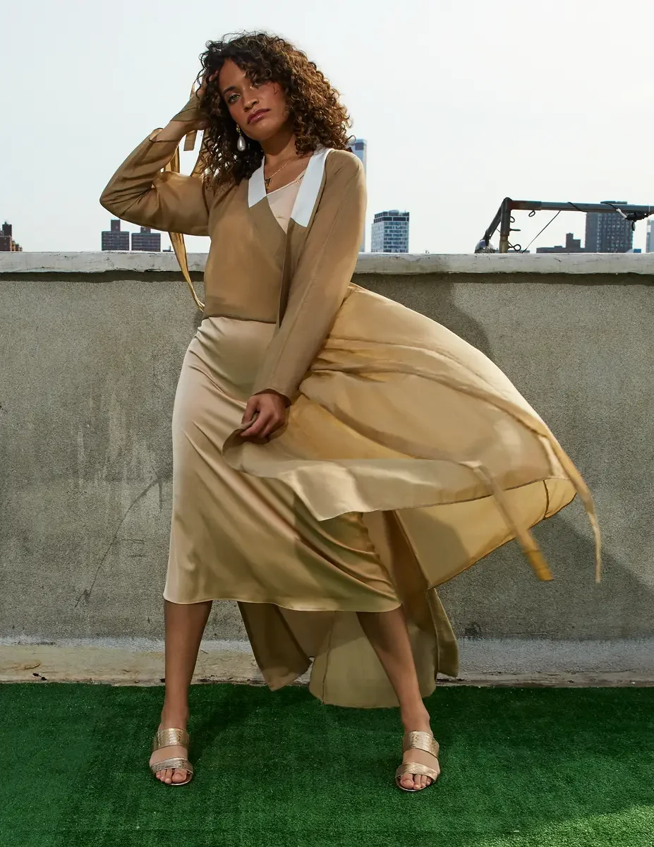 Fashion test shoot, full-length, model Ireland T in a gold satin wrap dress with white collar detail, skirt lifting in the wind, Manhattan skyline, East Village rooftop, New York City, styling by Matsine Stinson, makeup by Stefani Paige Vivian, photo