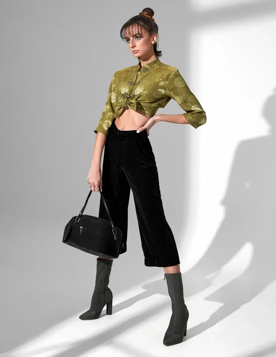 Model Macy, full length, three-quarter turn, olive green satin jacquard tied crop top with gold medallion print and frog closures, black wide-leg ribbed velvet culottes, olive green block-heel sock boots, black suede barrel bag, New York studio test 