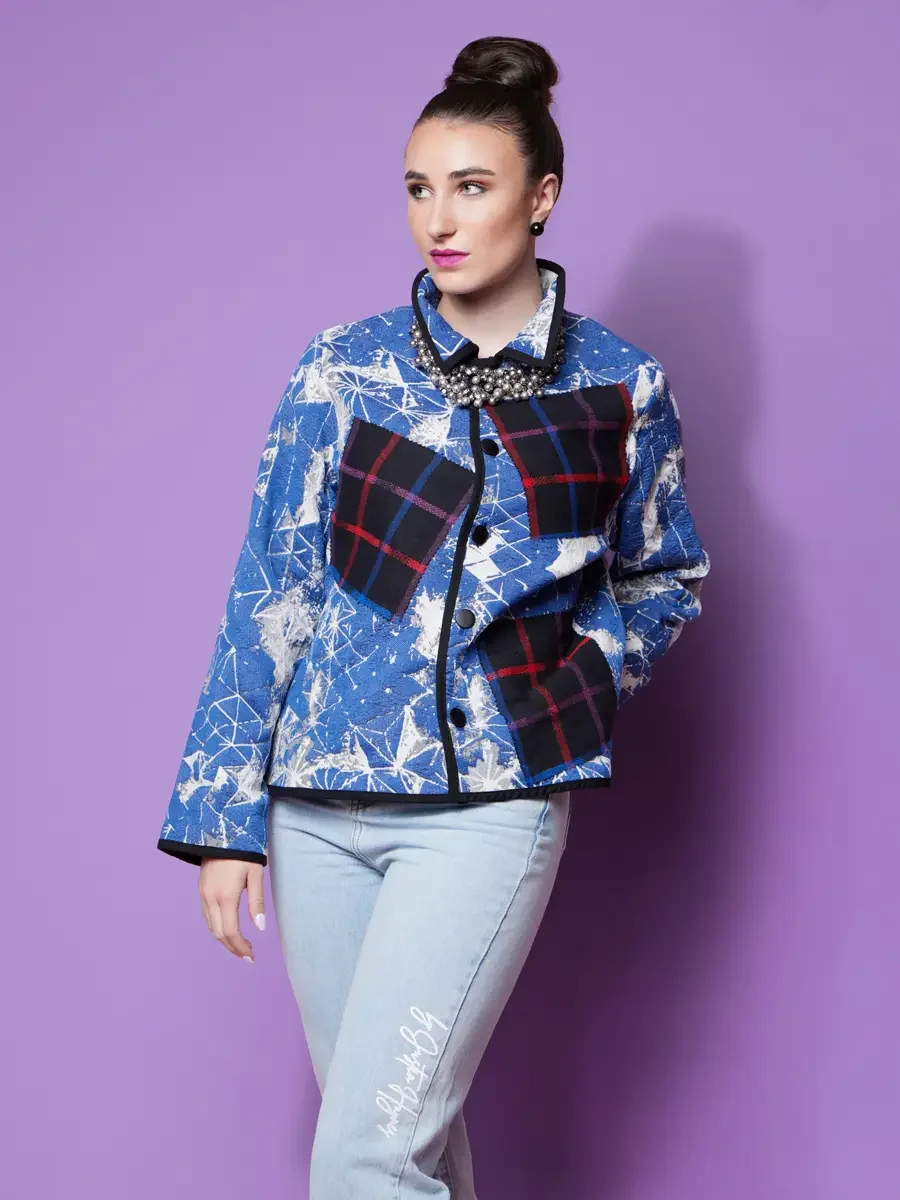 JUS10H 2025 Nylon Japan feature, close-up three-quarter shot, model in blue snowflake and geometric print cropped jacket with navy tartan patchwork panels and crystal collar necklace, light blue JUS10H script jeans, lavender background, photographed 