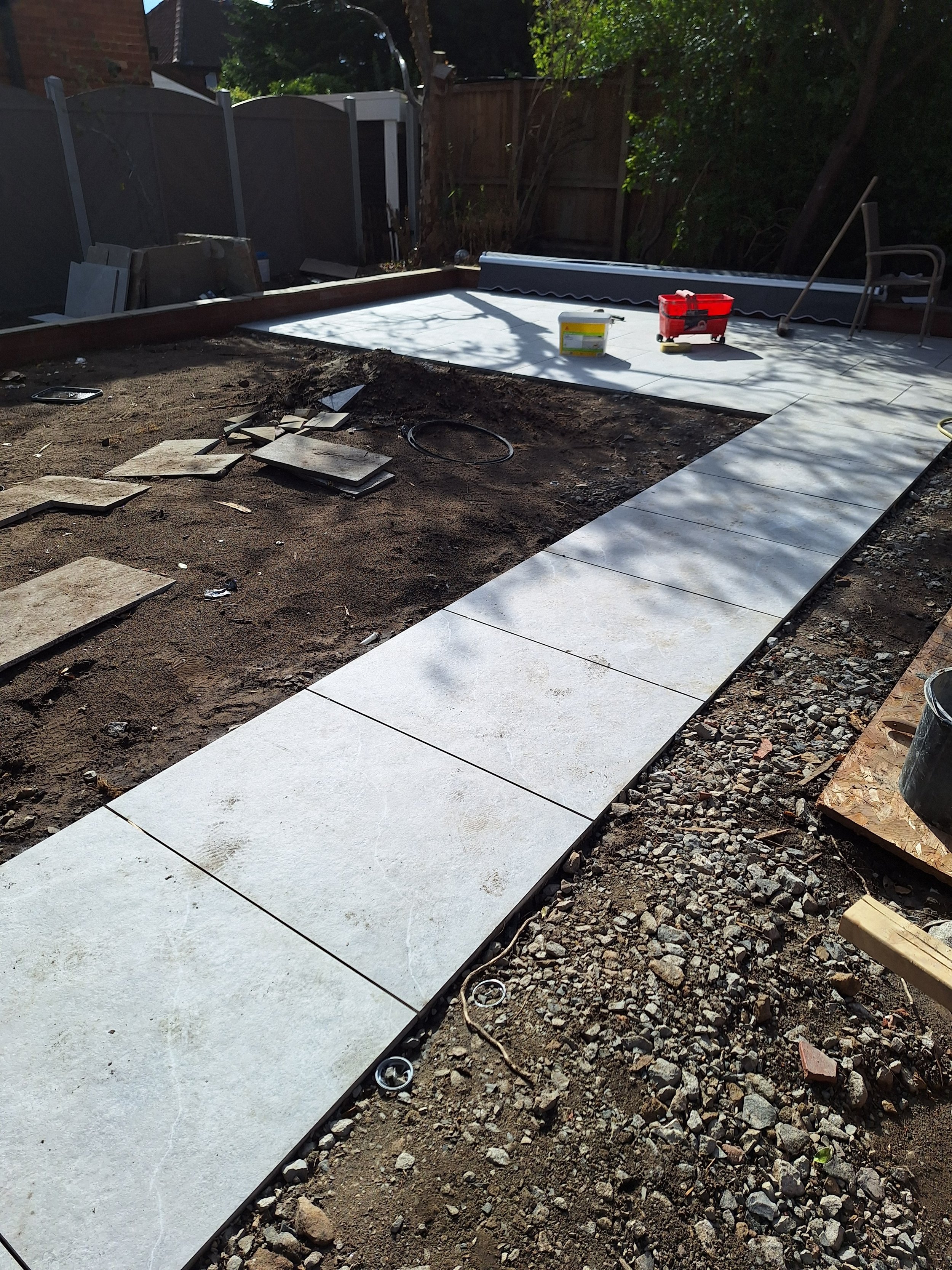 Construction site with newly laid concrete pavers forming a pathway, surrounded by dirt and gravel, with construction tools and materials nearby.