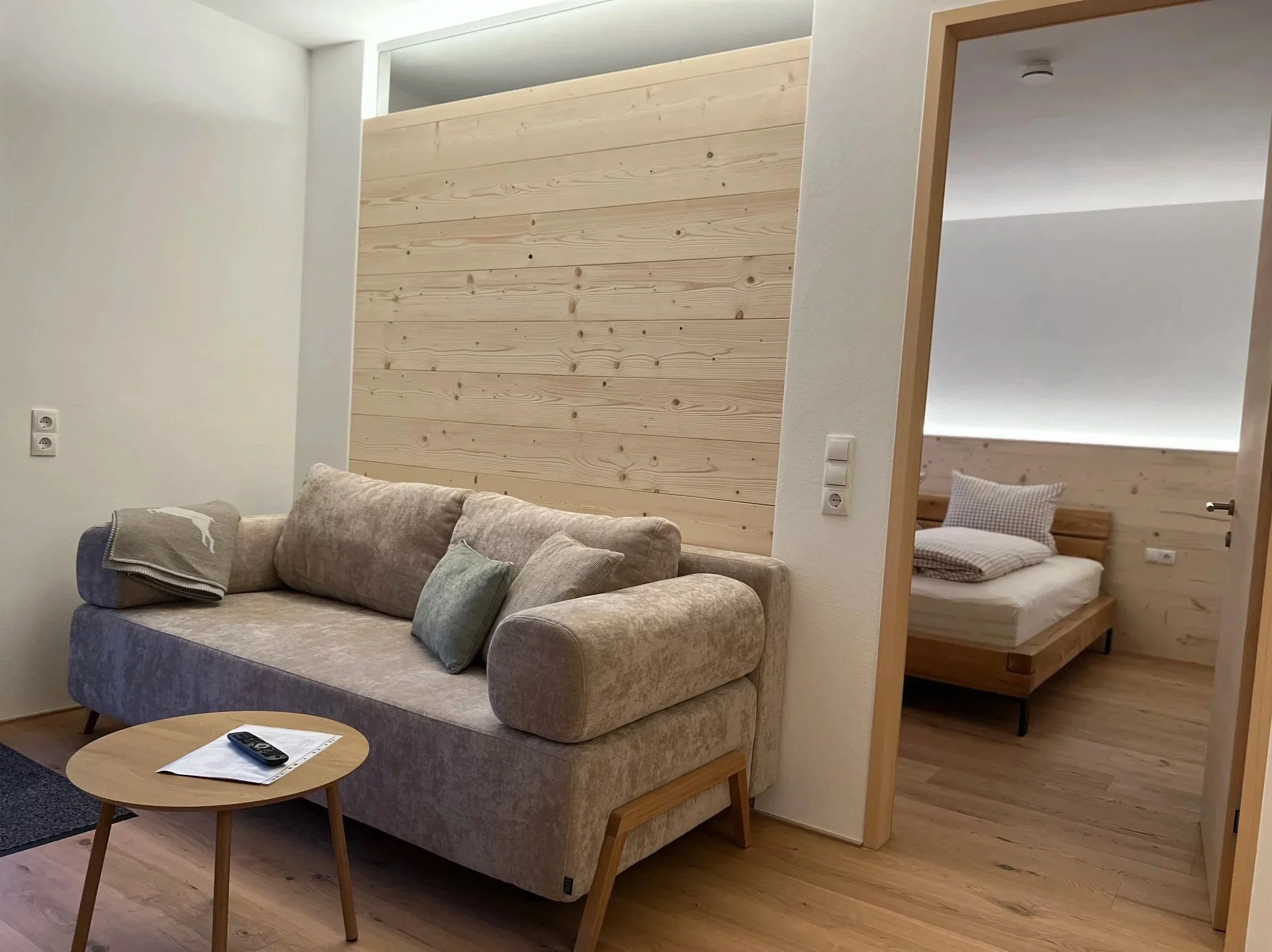 Wohnzimmer mit Couch, kleinem Tisch und Blick auf ein Schlafzimmer mit Doppelbett