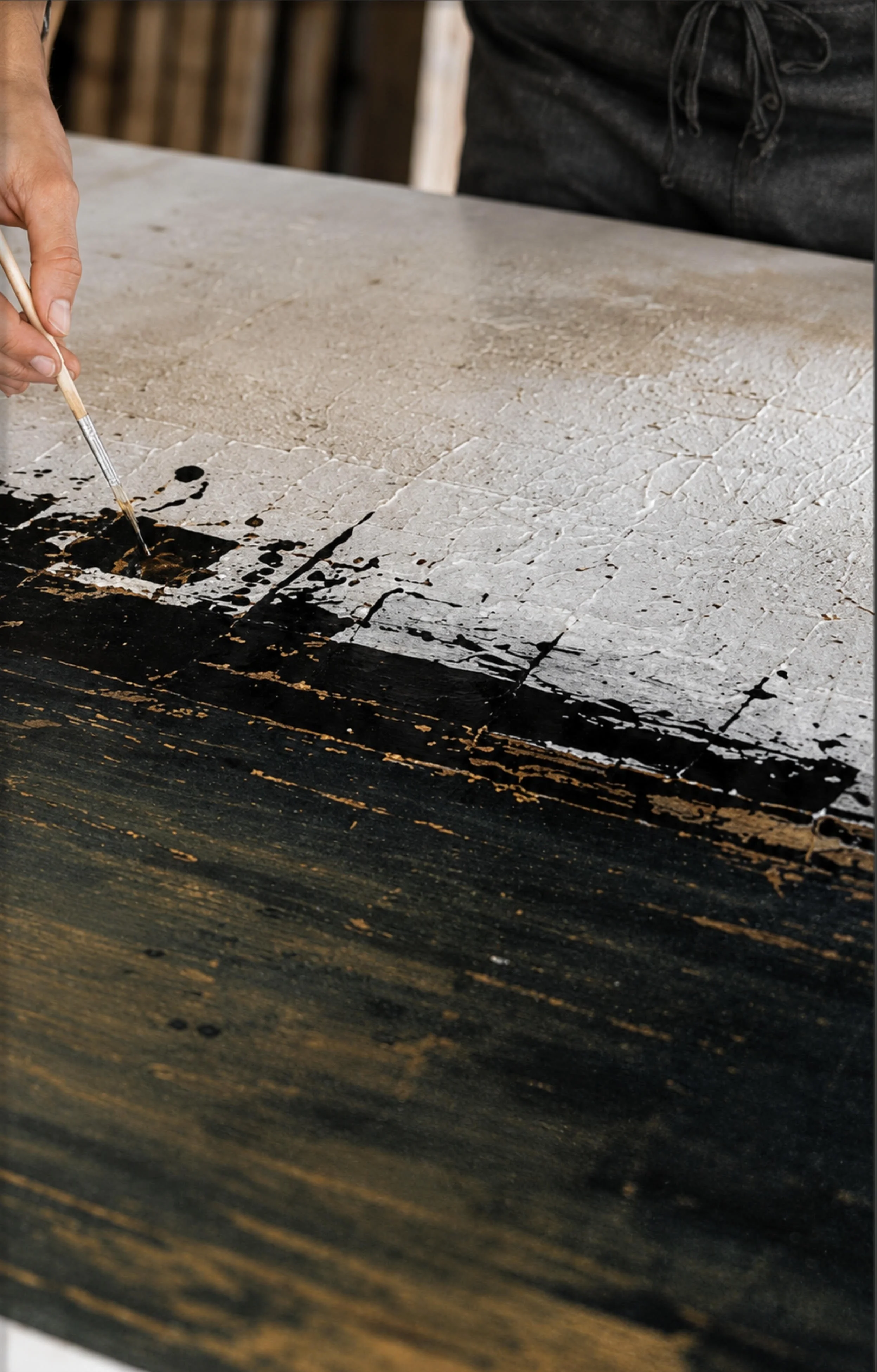 Close-up of a person painting a black and gold abstract design on a wooden surface with a fine brush.