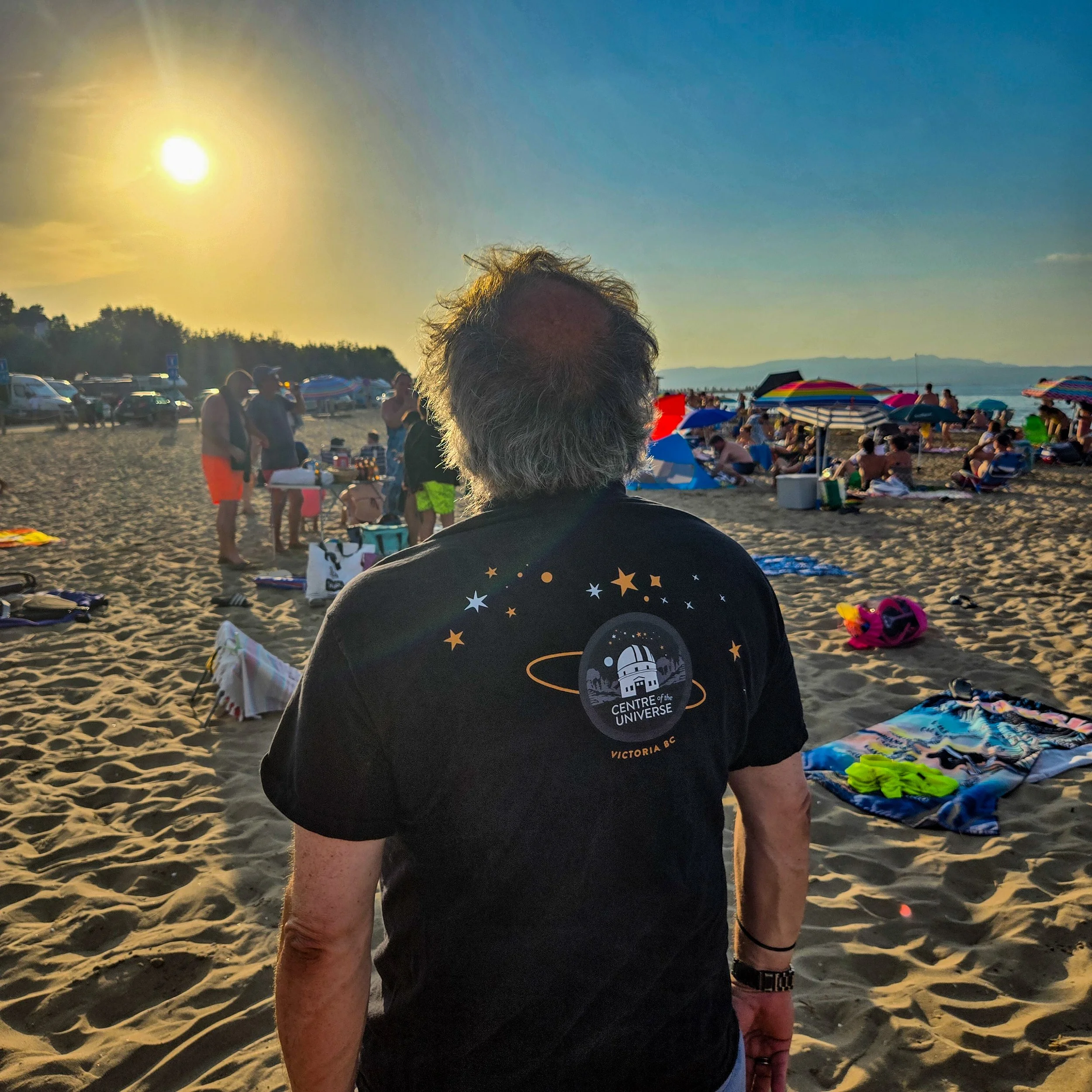 Man wearing Centre of the Universe T-shirt looks at the sun at a beach before the eclipse starts