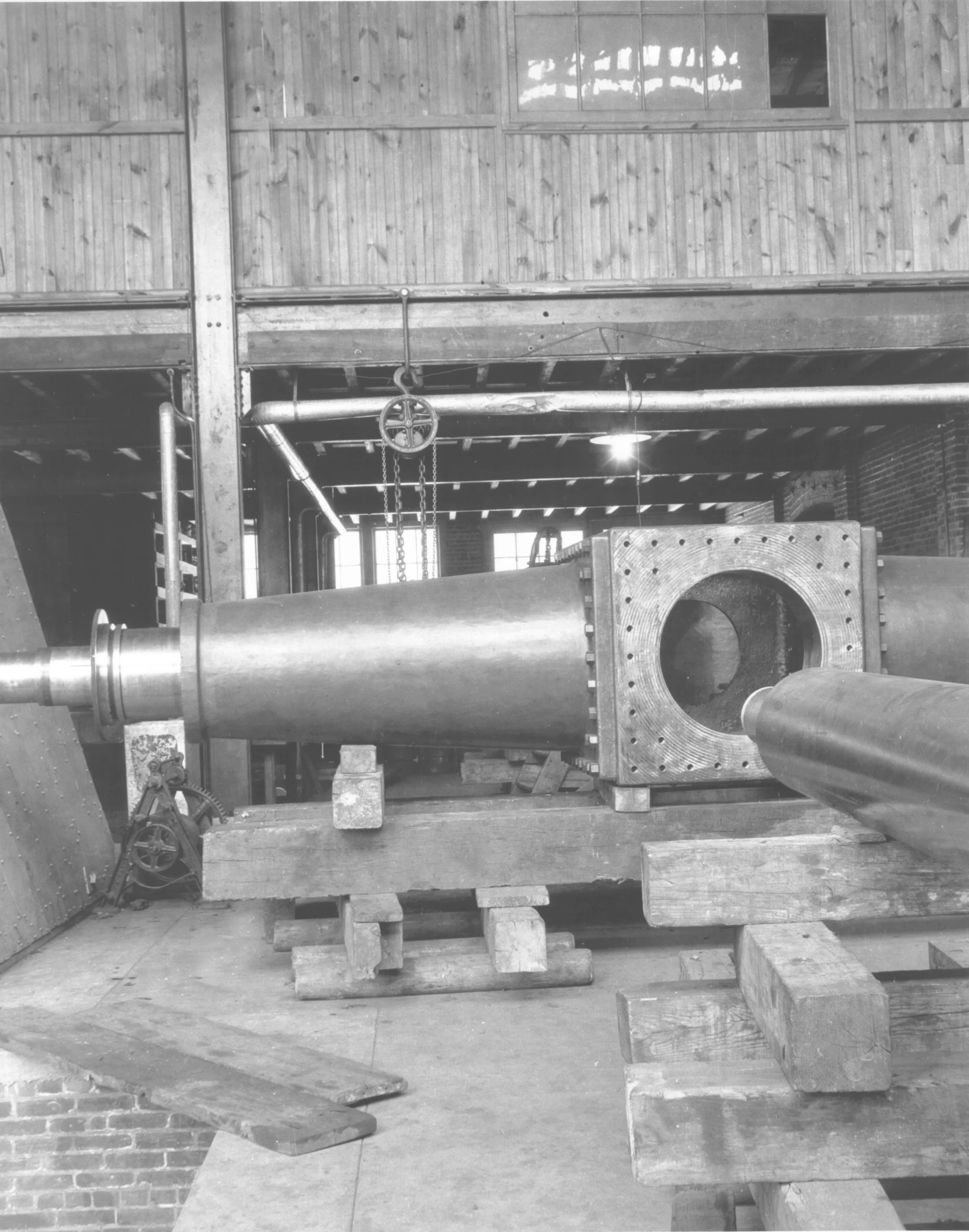 Large industrial pipe placed on wooden supports inside a warehouse.