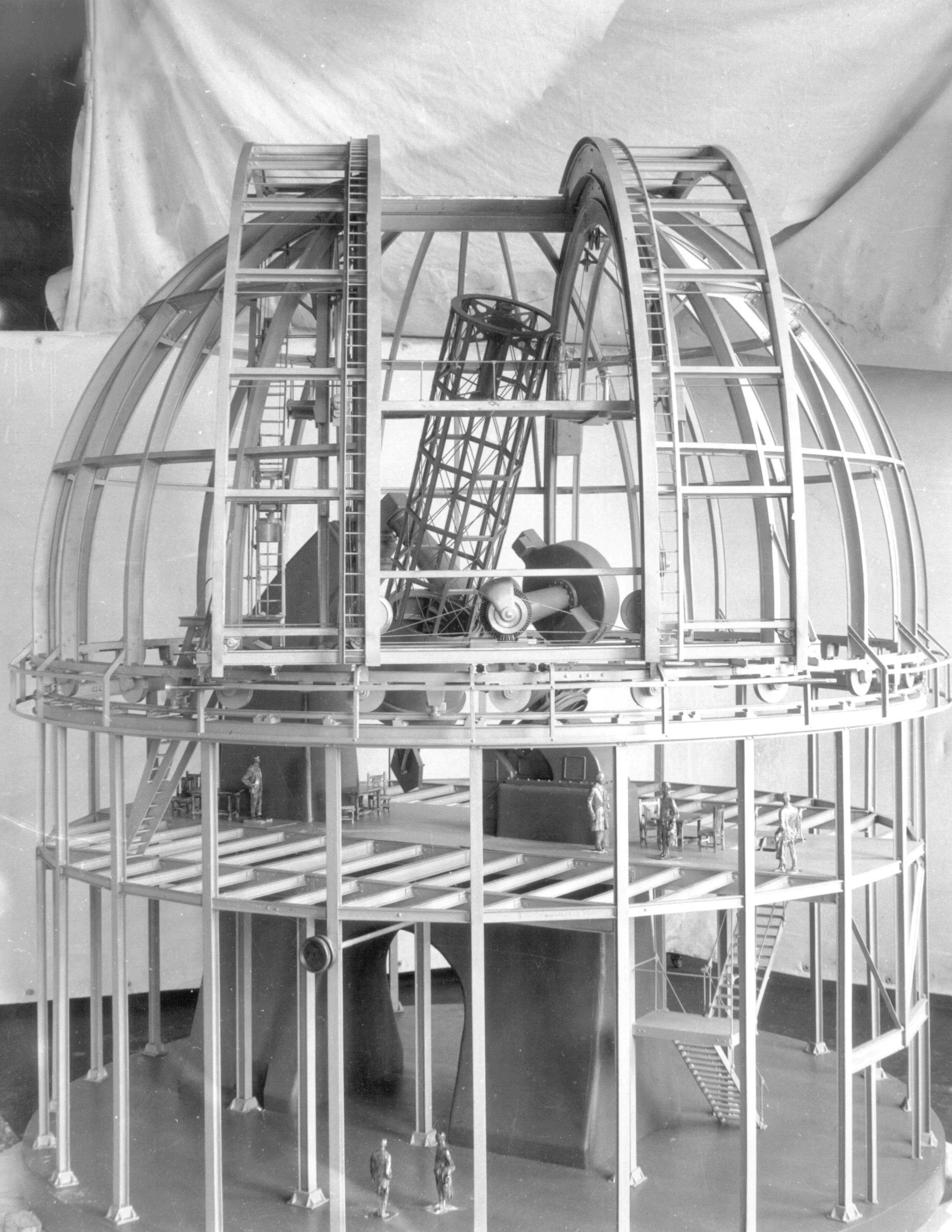 Model of an observatory dome with telescope and scaffolding, featuring small figures for scale.