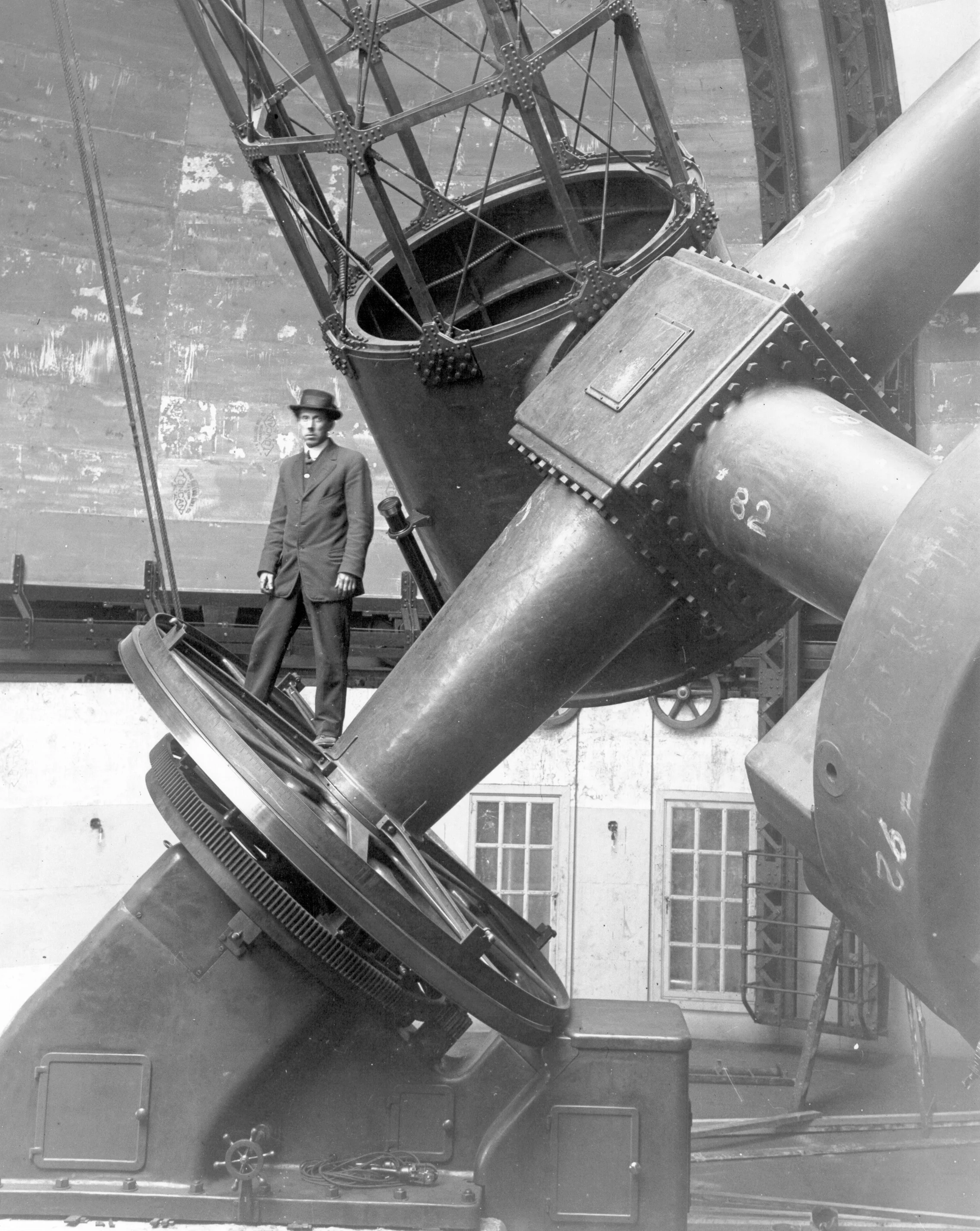 Black and white photograph of a man standing inside a large industrial or scientific machine with pipes, tubes, and metal framework, possibly a rocket or missile engine or similar equipment.