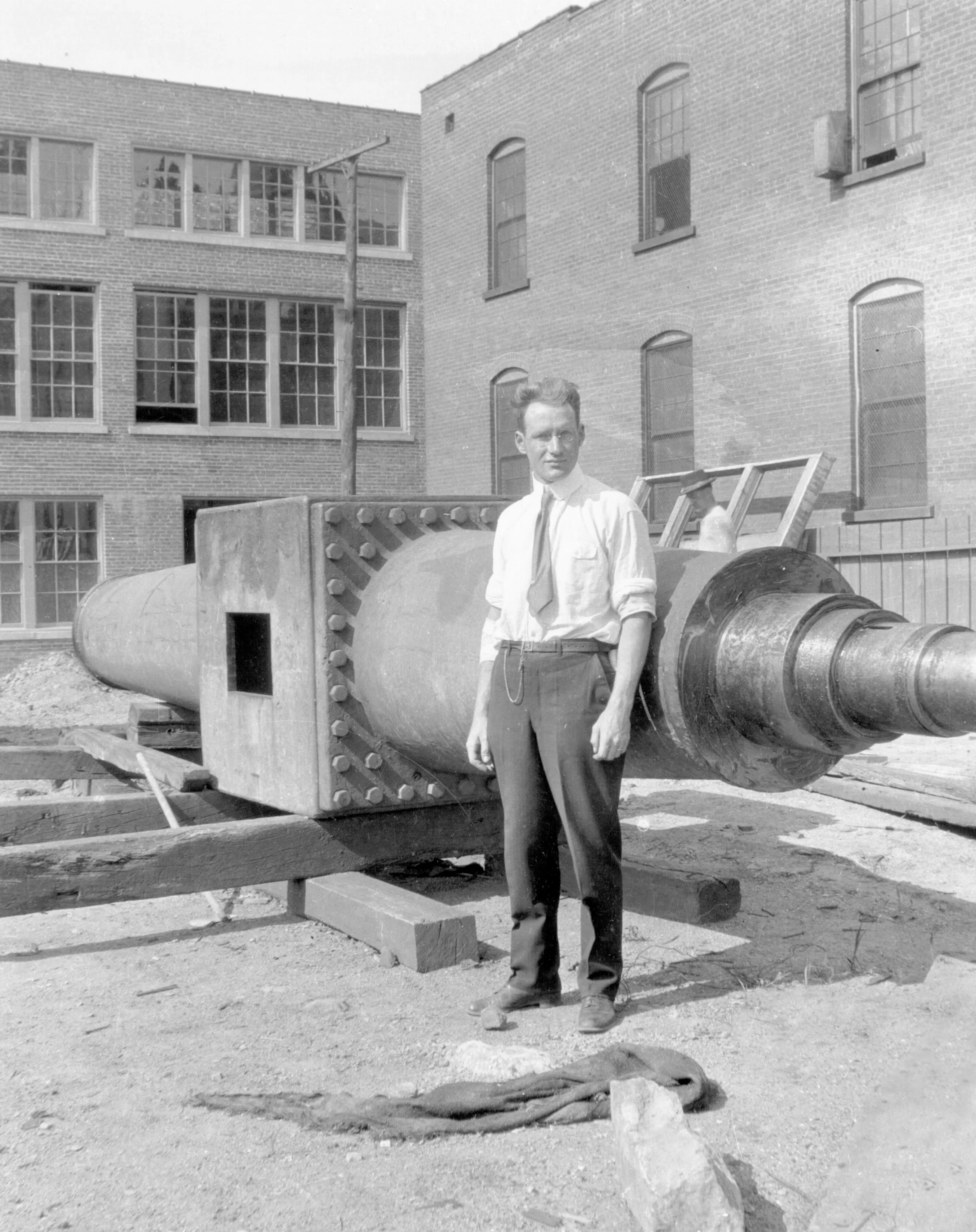 Man standing in front of large industrial machinery outdoors near brick building