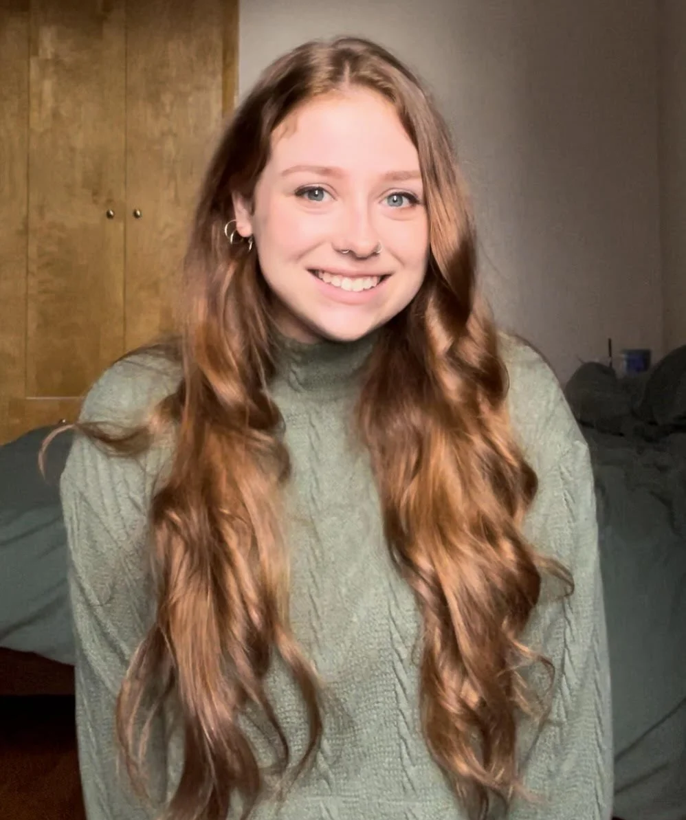 A woman with long, wavy hair wearing a green sweater and smiling.