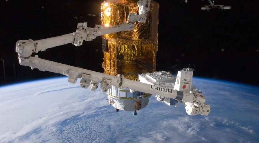 The image shows the Canadarm2, a robotic arm on the International Space Station, with Earth visible in the background.