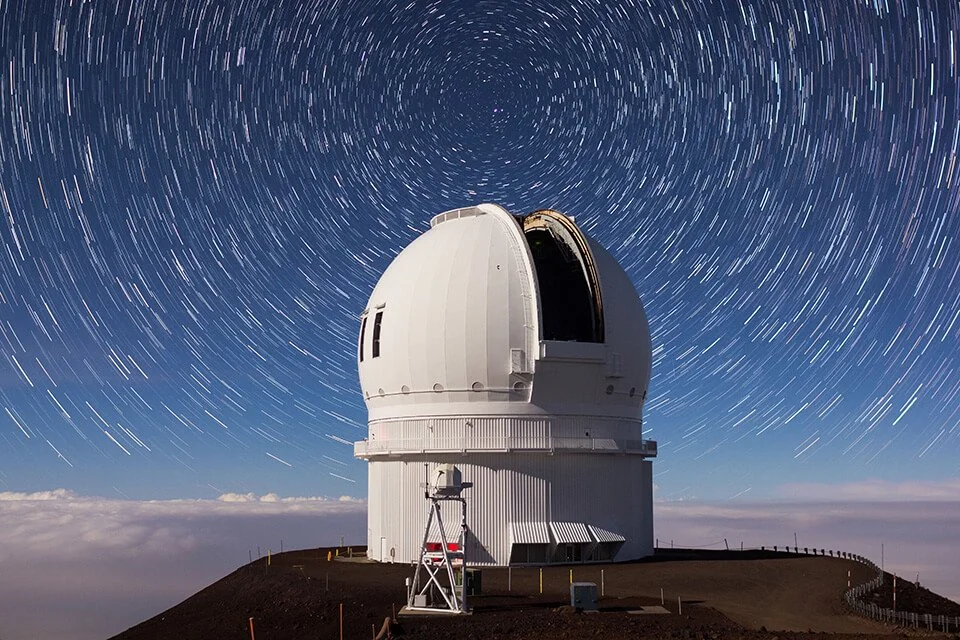 Long-exposure photo of the Canada France Hawaii Telescope on Mauna Kea, Hawai'i, under a starry night sky with star trails.