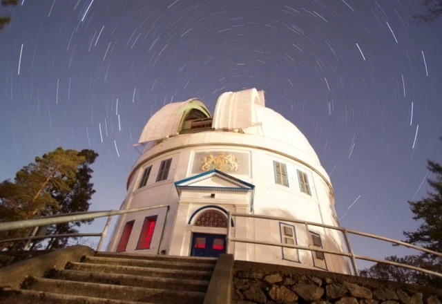 The Griffith Observatory at night with star trails in the sky above.