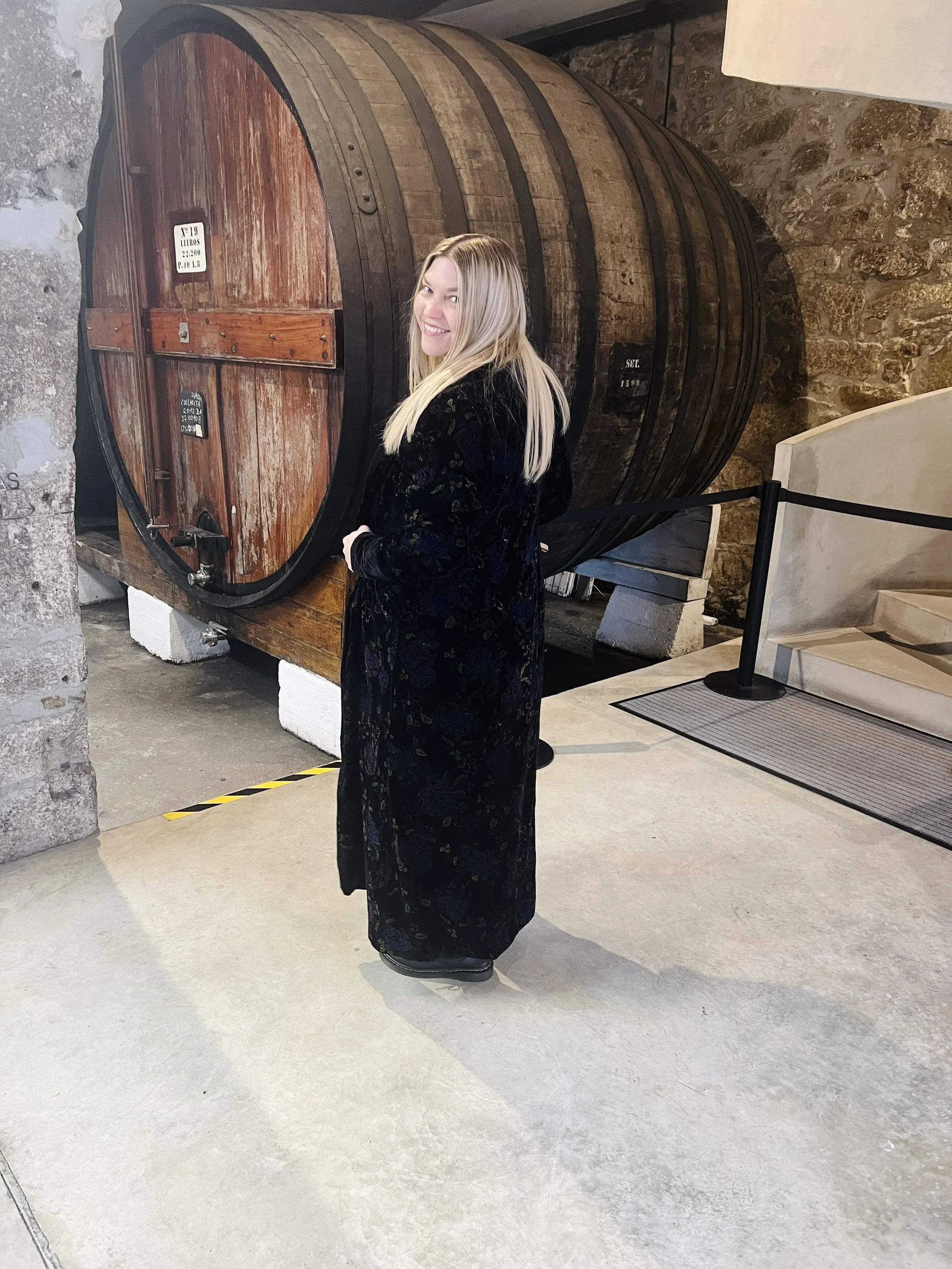 Anna Johnson standing inside a historic stone building beside a large wooden wine barrel.