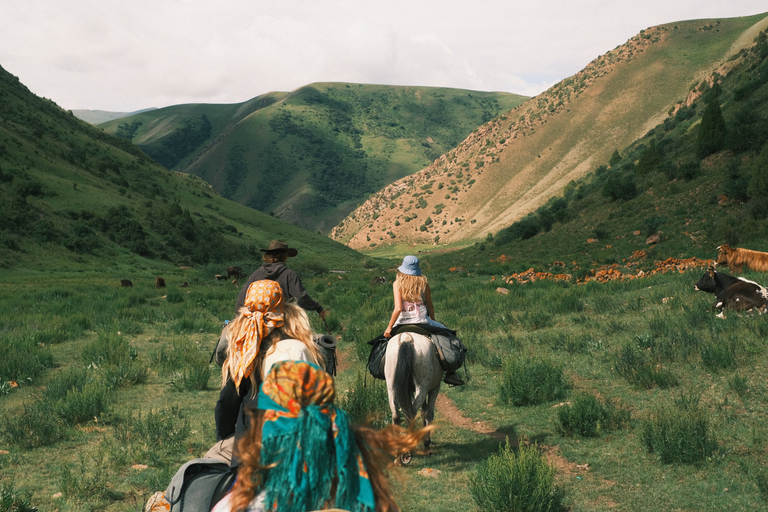 A group of people riding horses through a green valley surrounded by rolling hills.