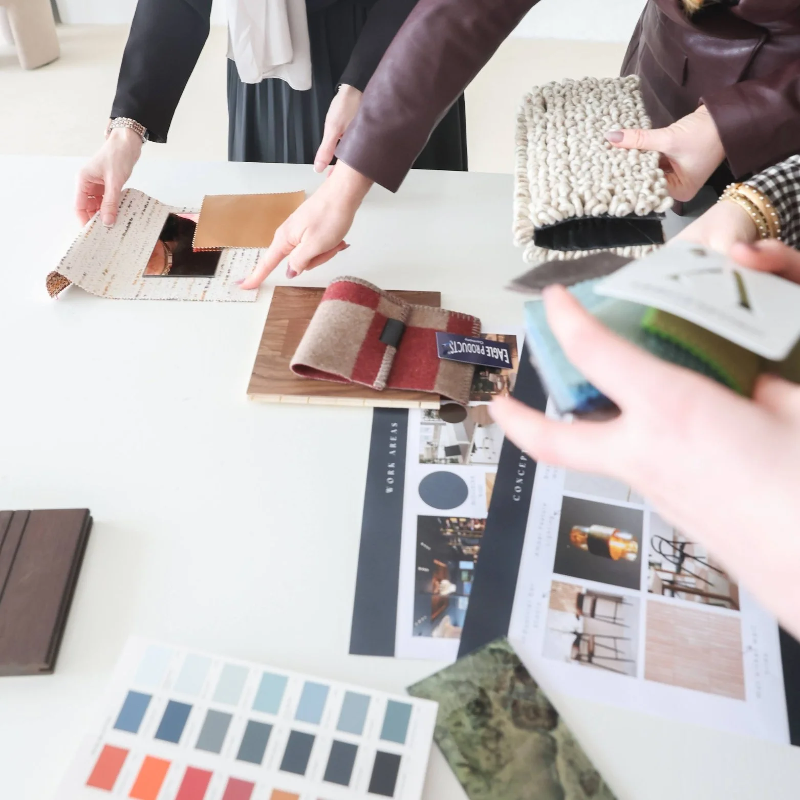 People reviewing fabric samples, paint swatches, and interior design magazines on a table.
