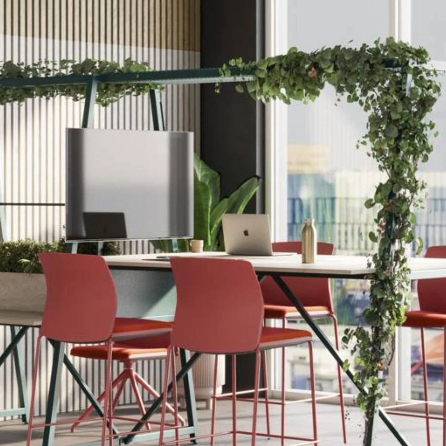 Modern office or meeting room with a table, pink chairs, laptop, plant, and decorative greenery arch near large windows.