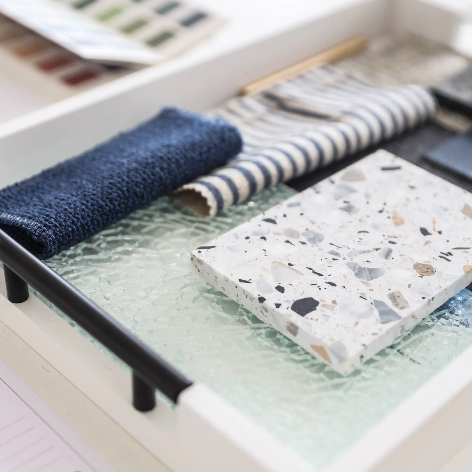 Sample materials including navy blue and striped fabric swatches, patterned tile, and paint color palette on a glass surface display.