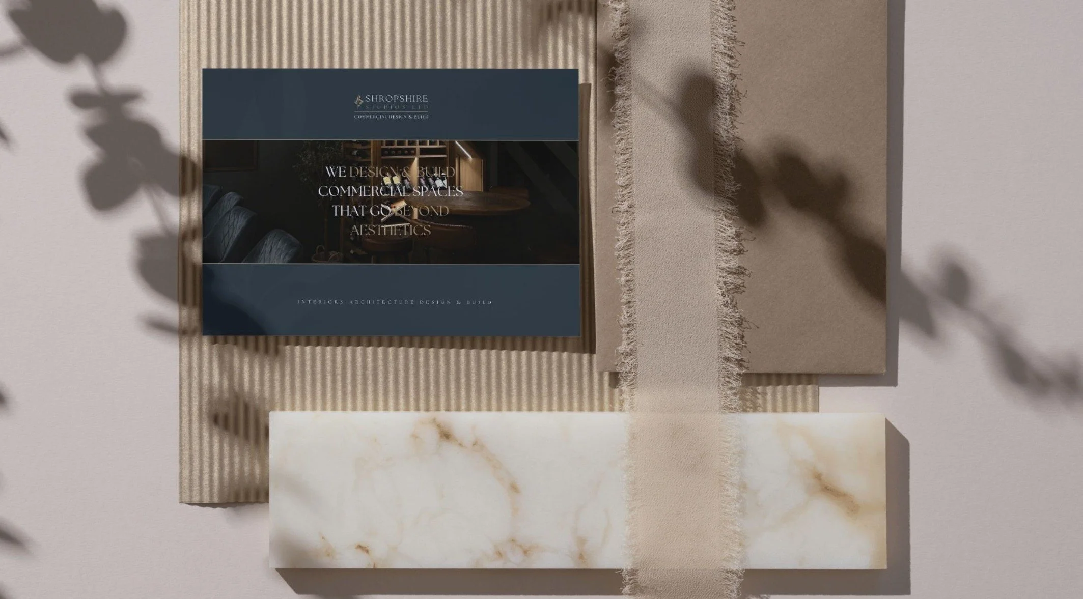 A promotional display with design elements for a company called Shropshire Plus Ltd, featuring a brochure, textured materials, a marble slab, and shadows of leaves on a light background.