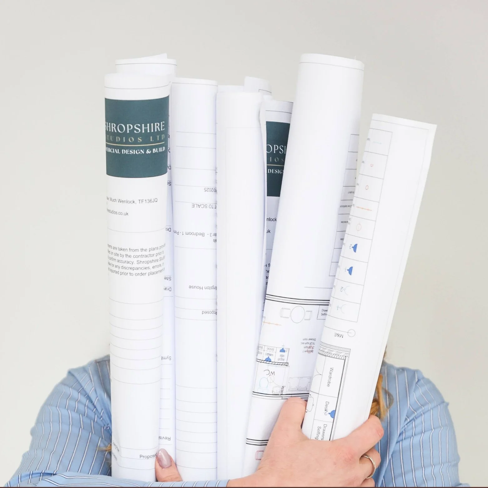 Person holding multiple rolled-up architectural plans and blueprints.