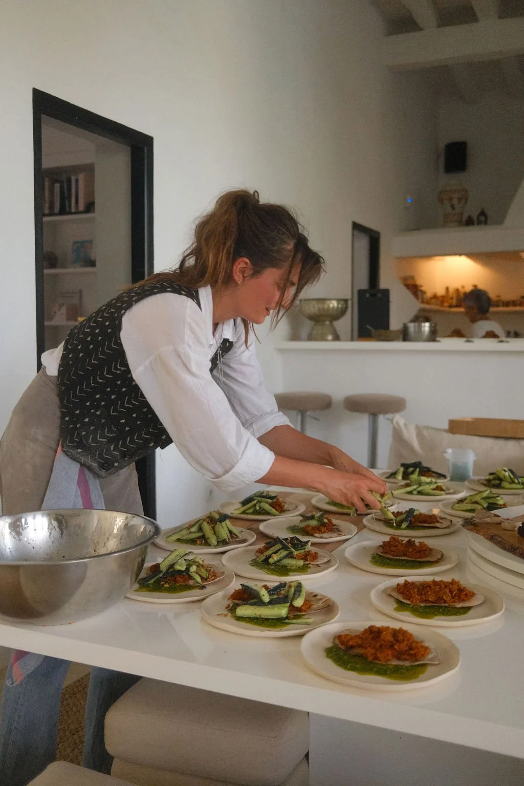 Frau bereitet mehrere Teller mit Essen in einer modernen Küche vor.