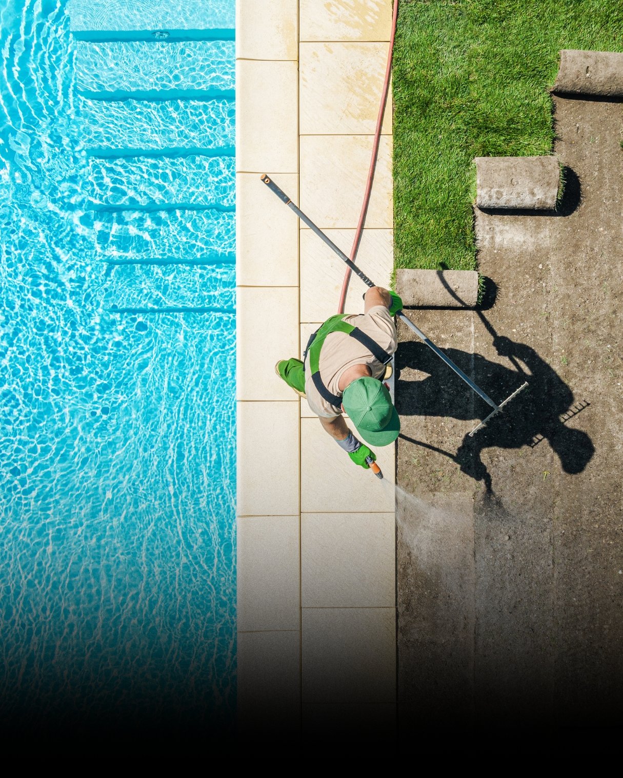 Mann, der den Poolbereich reinigt, mit Wasser-Schlauch, neben Gras und Pflastersteinen, über Kopfansicht.