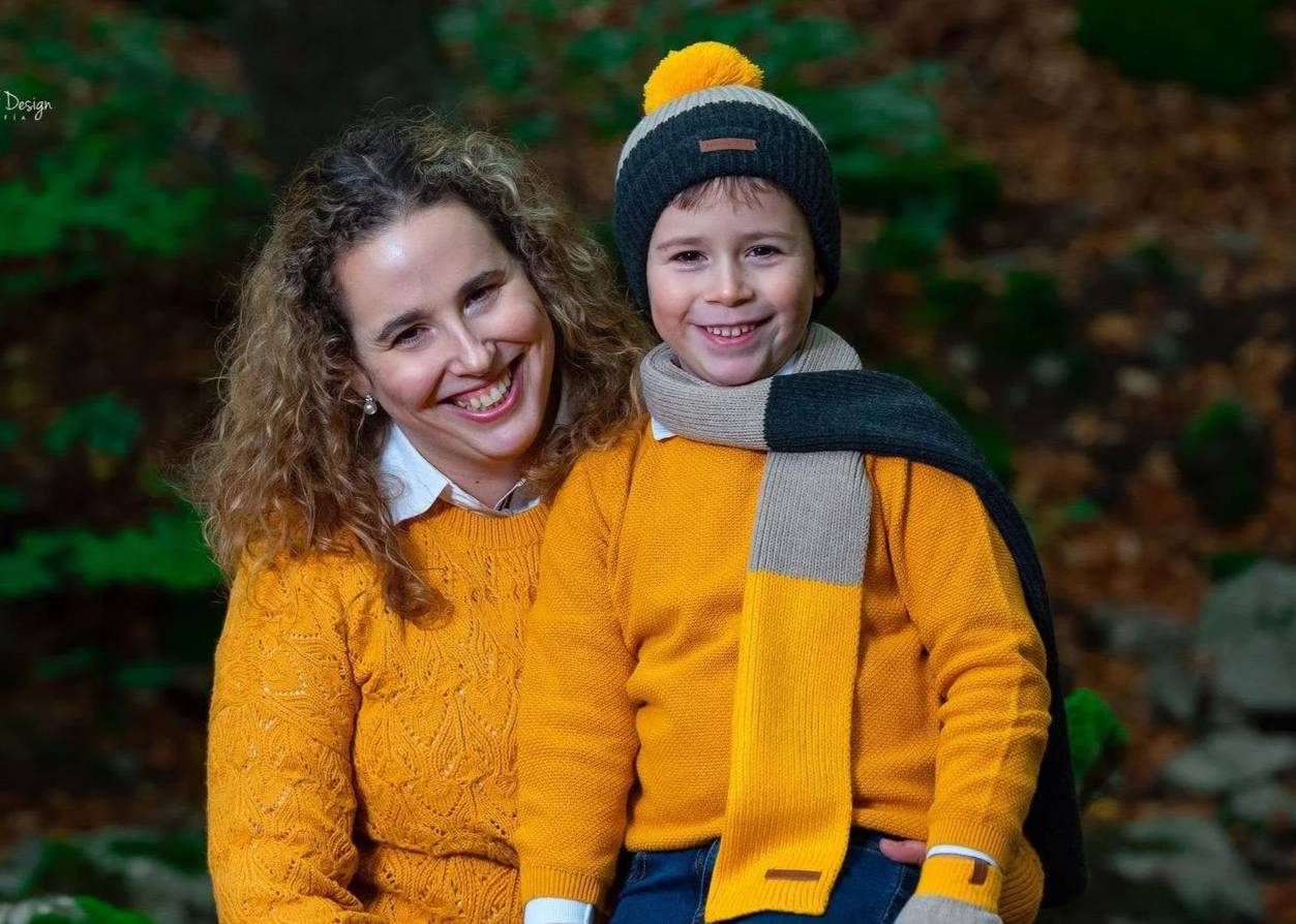 Una mujer y un niño sonriendo en un bosque, vestidas con ropa color mostaza y accesorios de invierno.
