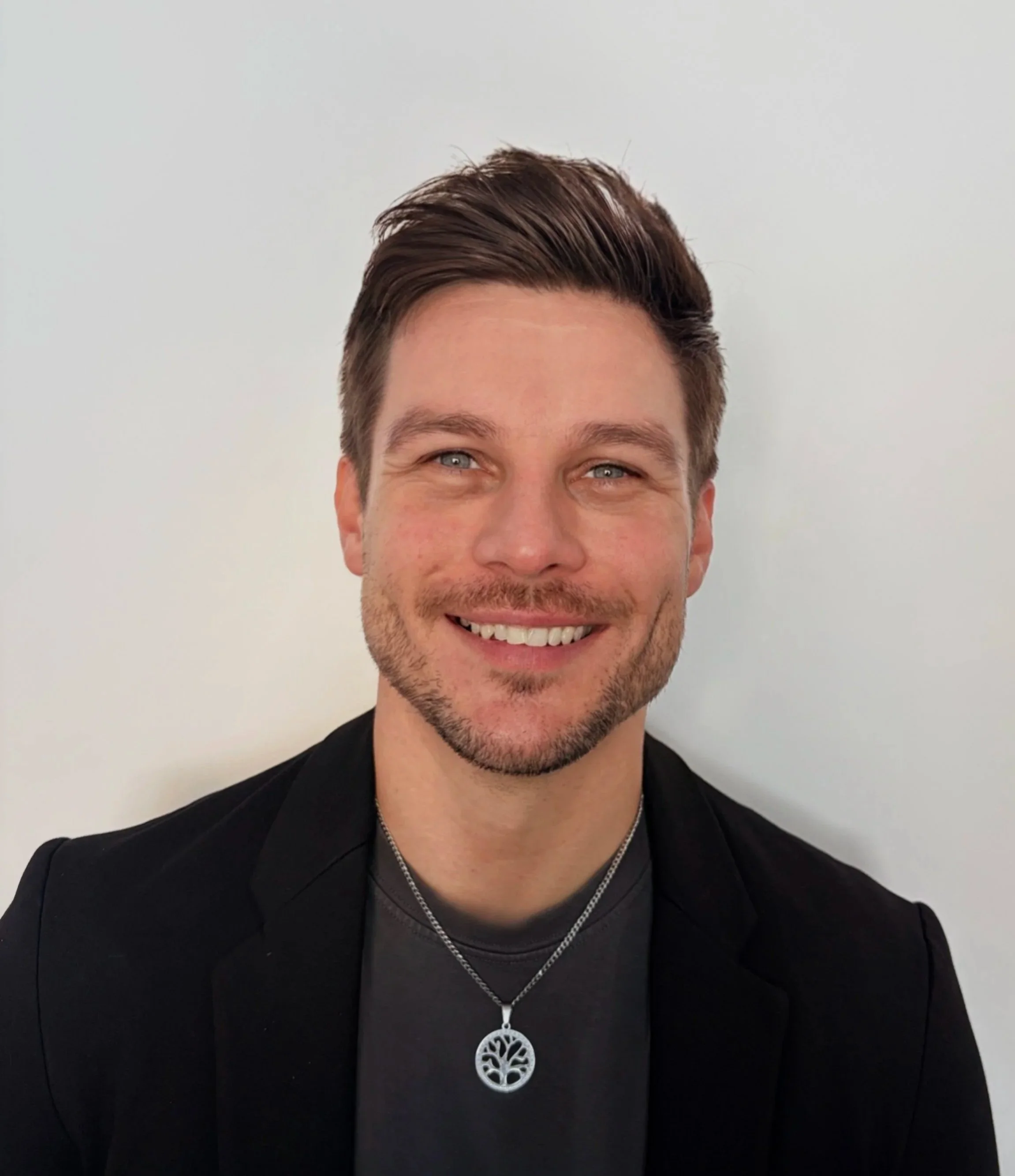 Retrato de un hombre con barba, gafas transparentes, y cabello rizado oscuro, en un ambiente interior.
