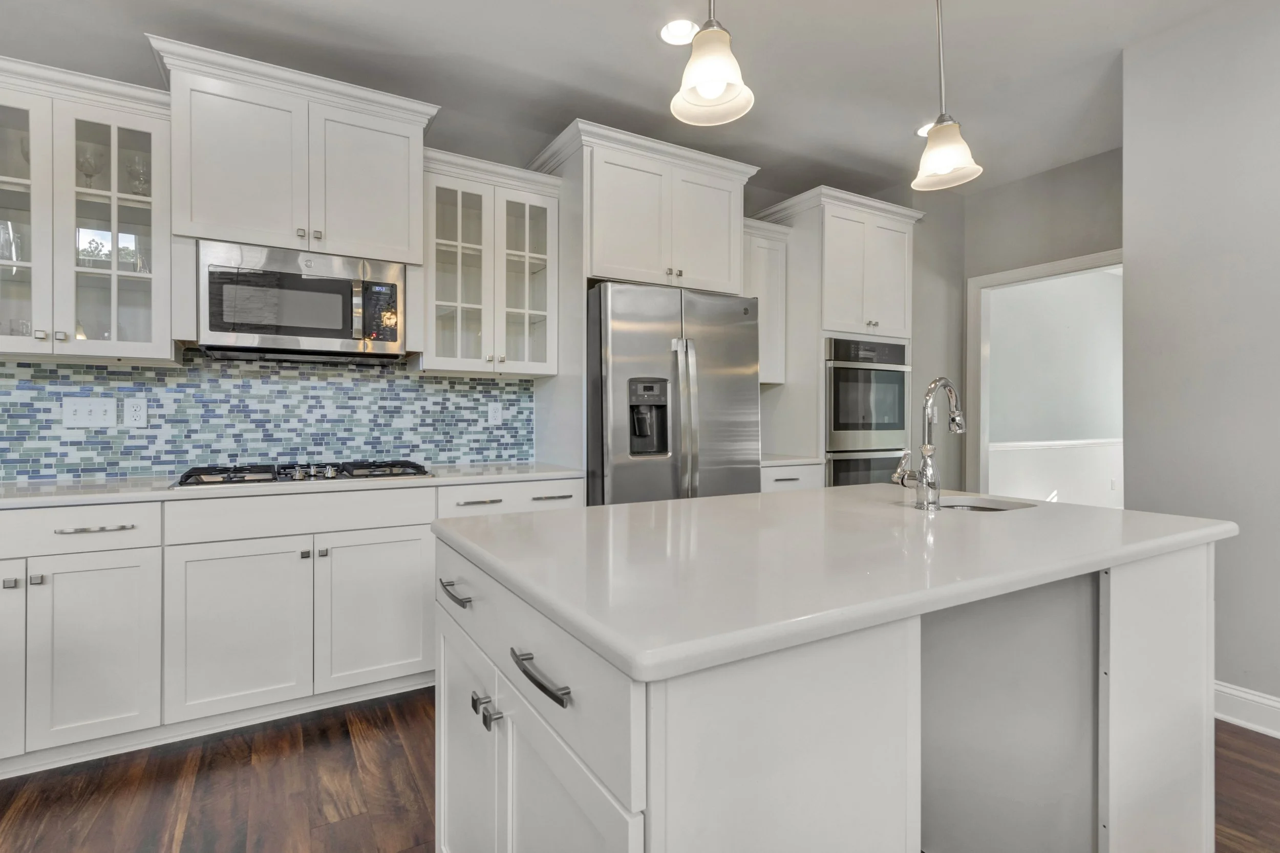 Modern kitchen with white cabinets, a kitchen island, stainless steel refrigerator, microwave, and oven, mosaic tile backsplash, and hardwood floors.