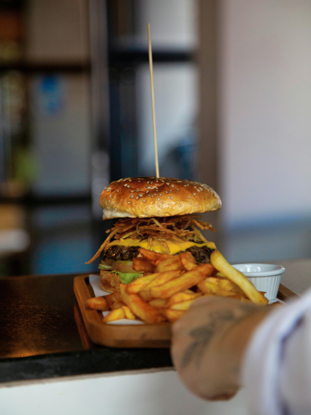 Close-up of a cheeseburger with fries and dipping sauce on a wooden tray.