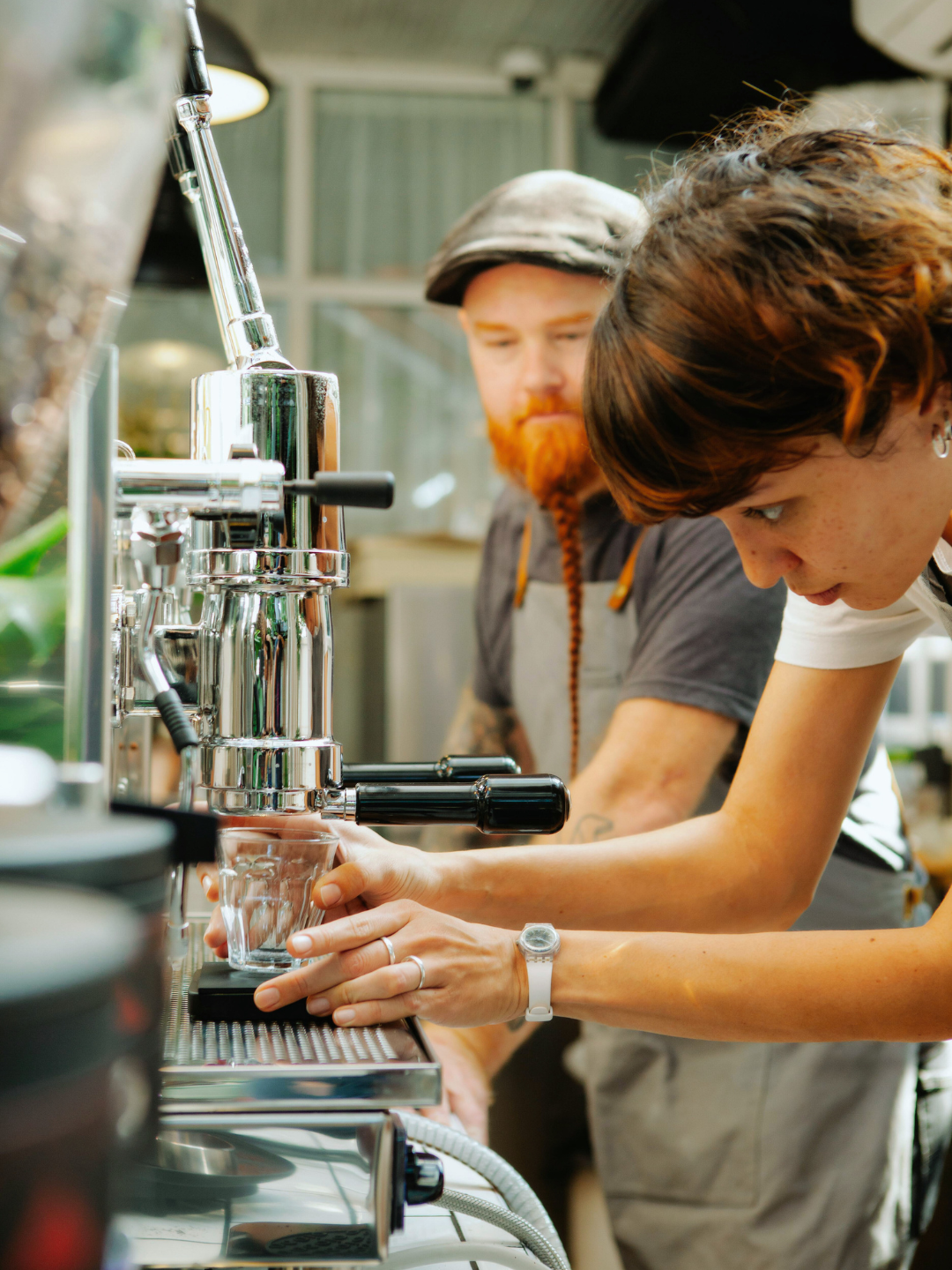 Two people preparing coffee using an espresso machine in a café or kitchen setting.